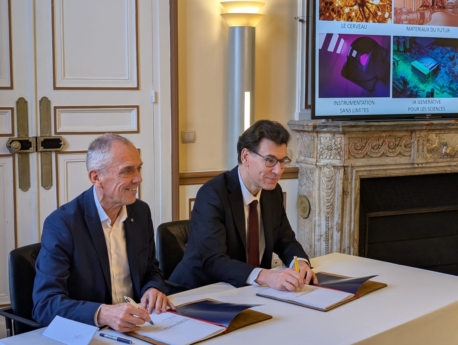 Antoine Petit and Philippe Baptiste signing a document at a table