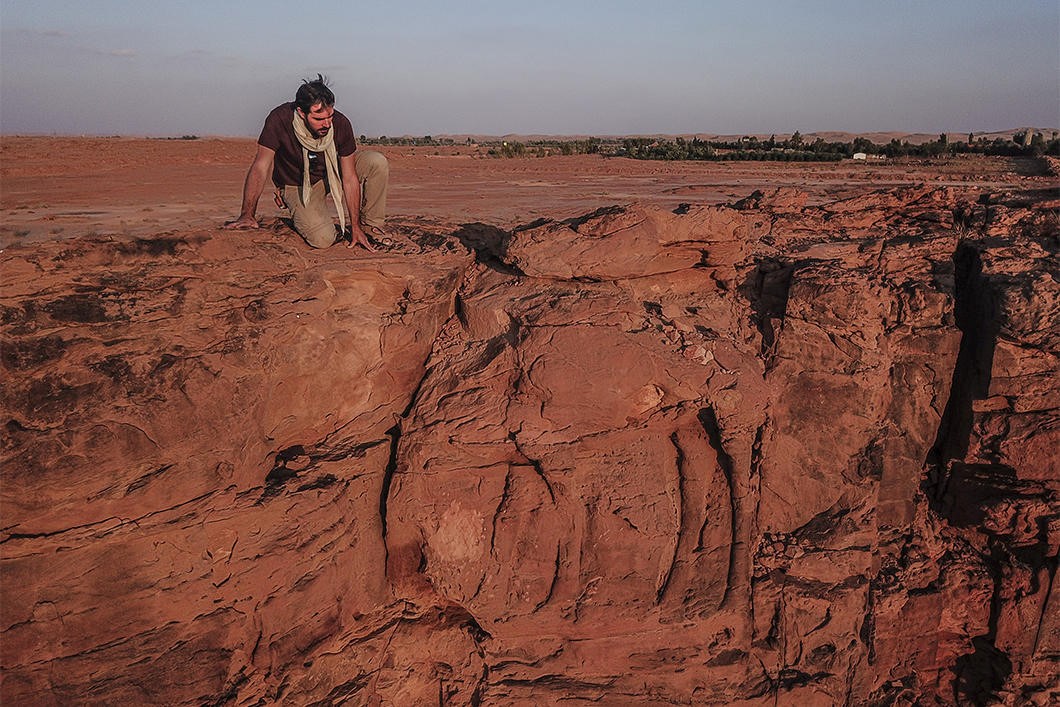 un chercheur sur l'un des promontoires rocheux : un dromadaire est gravé dans la paroi verticale. On distingue ses pattes et son tronc mais la tête a été abimée par l'érosion.