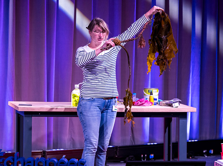 Une chercheuse sur la scène de la Cité des sciences montre une algue au public