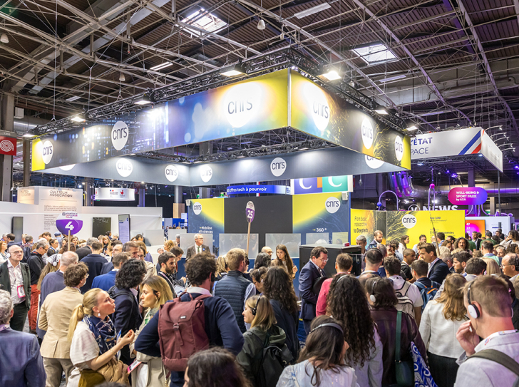 CNRS stand at VivaTech 2024 ; indoors during the day, a crowd of people are walking in front of the stand, we can see the ceiling with several metal structures and square windows
