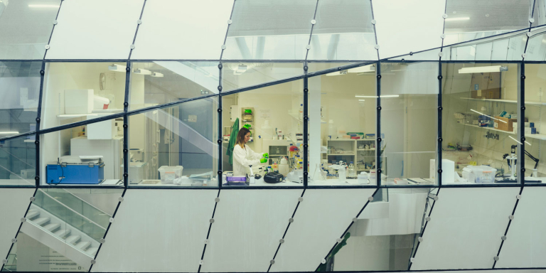 Une chercheuse en blouse blanche vue à travers les vitres du laboratoire interdisciplinaire de neurosciences